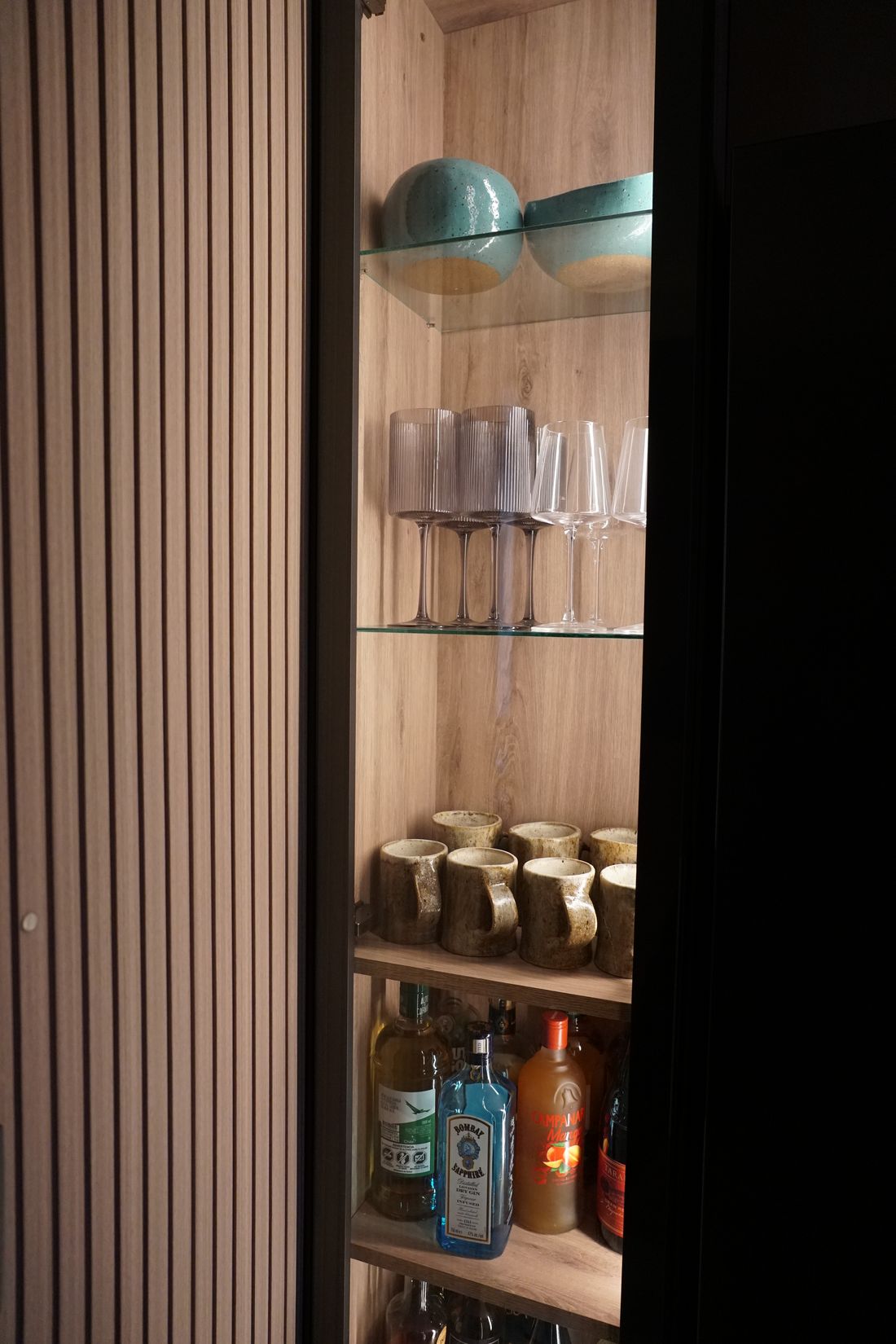 Cocina con muebles de madera, cubierta negra y luz lineal bajo los muebles altos