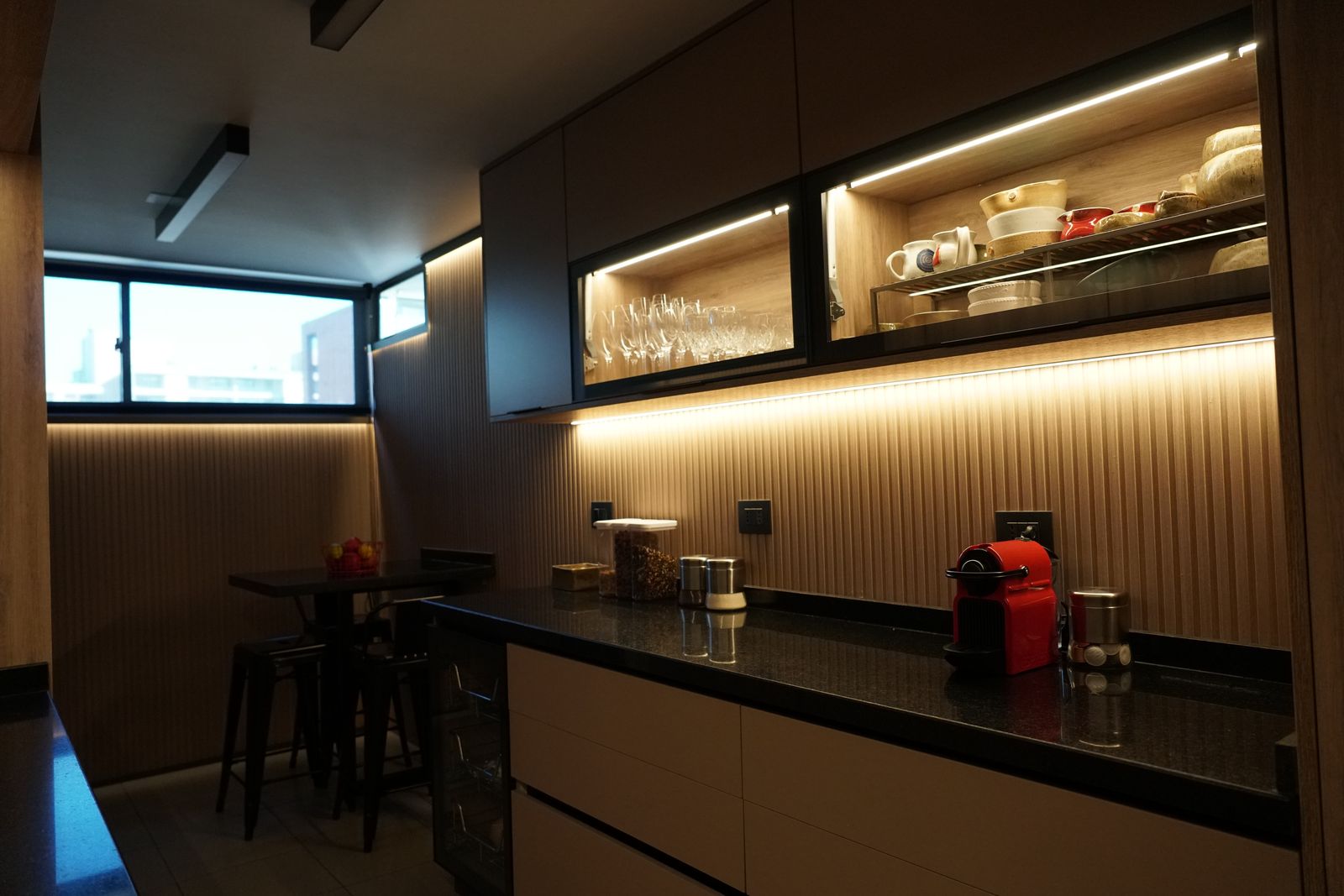 Cocina con muebles de madera, cubierta negra y luz lineal bajo los muebles altos